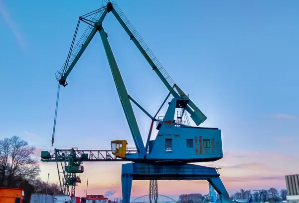 Industriekulisse im Niehler Hafen: Historischer Kran in Köln vor blauem Himmel in den Abendstunden.